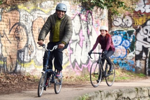 Couple wearing helmets cycle down the side of a canal in line