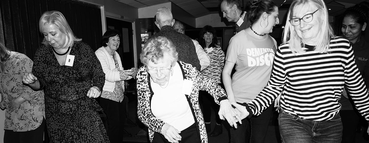 Men and women of different ages smile as they dance indoors.