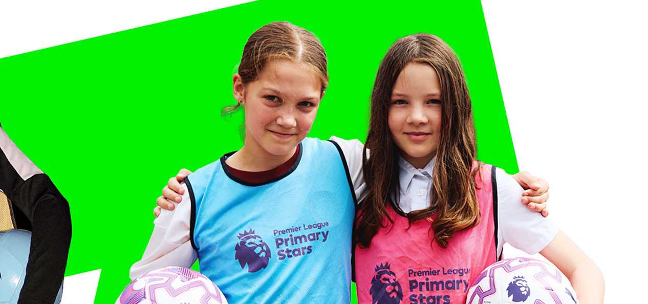 Two little girls stand side by side holding footballs under their arms and wearing bibs with the words "Premier League Primary Stats" on them.  