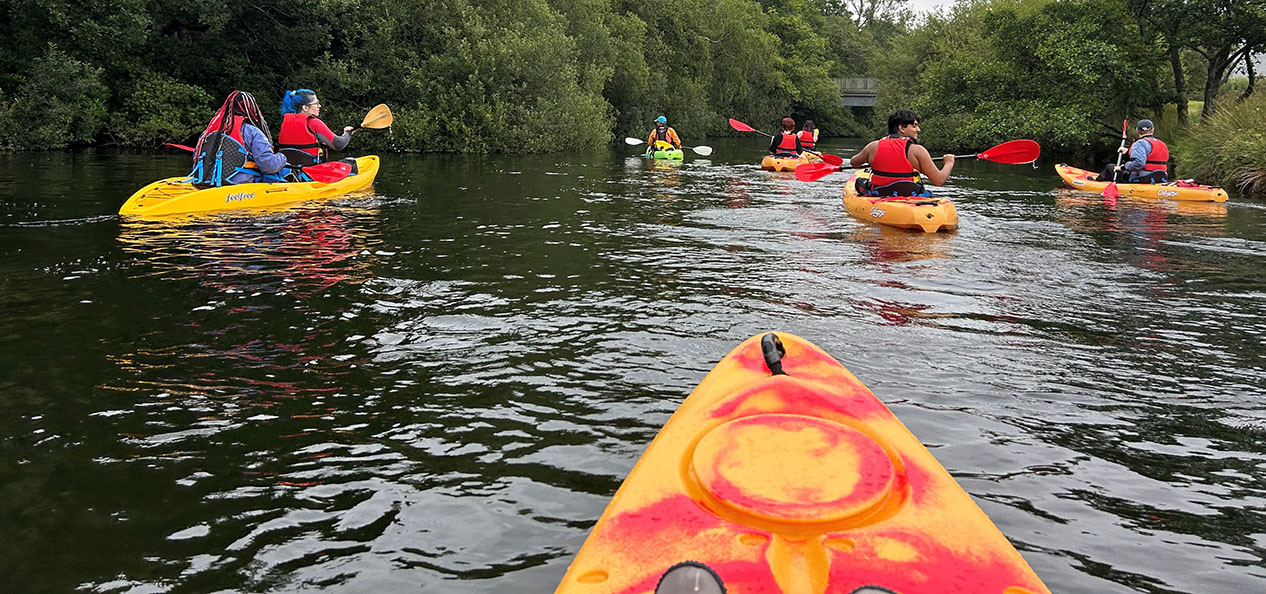 A group of kids go down the river on their kayaks on a lightly cloudy day.  