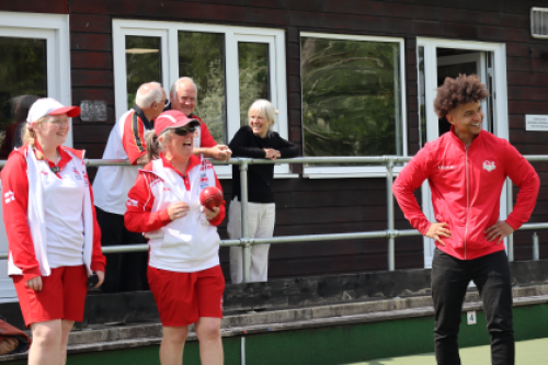 A group of bowlers wearing Team England kit laugh together on a green.